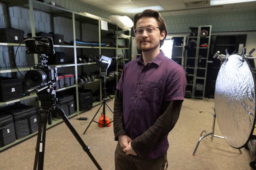 A video production student looks over film lights and camera.